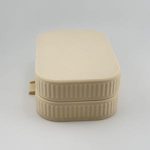 May include: A rectangular, beige-colored storage container with rounded corners and a ribbed, vertical-textured side design. The container features a flat, smooth lid that sits flush with the base, and a small, protruding tab on the left side.