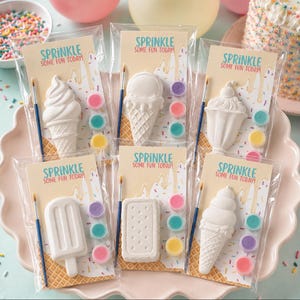 Puede incluir: Seis paquetes individuales de plástico transparente que contienen formas de helado de yeso blanco para pintar. Cada paquete incluye un pincel y tres pequeños botes de pintura, con una tarjeta que muestra el texto Sprinkle Some Fun Today.