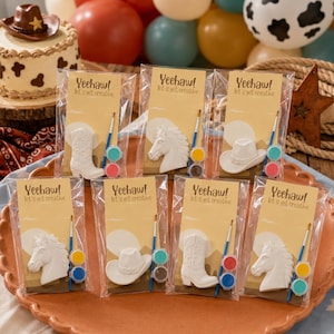 May include: Eight individual craft kits in clear plastic packaging, each featuring a white ceramic figure of a cowboy boot, horse head, or cowboy hat, a small paintbrush, and two paint pots, with a card labeled Yeehaw! let's get creative.