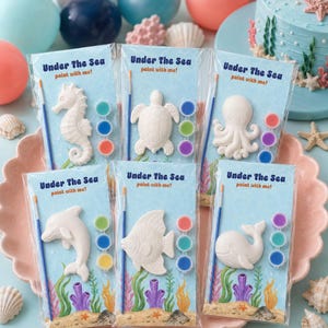 May include: Six individual clear plastic packages labeled Under The Sea paint with me, each containing a white sea creature figurine, a small paintbrush, and three paint pots. The creatures include a seahorse, turtle, octopus, dolphin, fish, and whale.