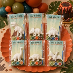 Puede incluir: Seis paquetes individuales de plástico transparente etiquetados como Roar & Explore Paint Your Own Dinosaur. Cada paquete contiene una figura de dinosaurio blanca sin pintar, un pincel azul pequeño y tres botes de pintura redondos.