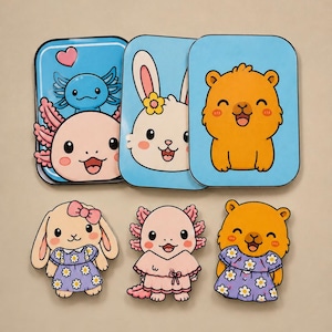 Pode incluir: Três cartões retangulares com fundos azuis apresentando axolotes, um coelho e um urso em desenho animado, combinados com três figuras recortadas de um coelho, um axolote e um urso, todos vestindo vestidos roxos com padrões de margaridas brancas.