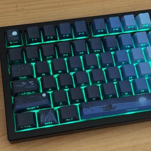 May include: A mechanical keyboard with a black frame and a gradient of blue keycaps. The keys feature custom illustrations of a night sky, mountains, and birds. The keyboard is illuminated by a bright green backlight that glows between the keys.