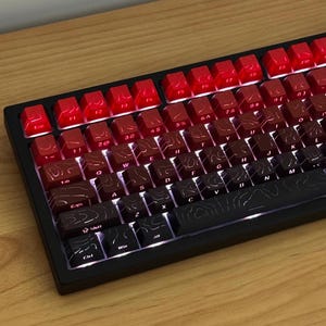 Könnte beinhalten: Eine mechanische Tastatur mit einem Farbverlauf der Tastenkappen, der von hellem Rot oben bis Schwarz unten reicht. Jede Tastenkappe zeigt ein topografisches Kartenmuster mit weißer Beschriftung und integrierter Hintergrundbeleuchtung.