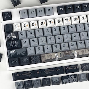 Puede incluir: Un teclado mecánico con marco blanco y teclas personalizadas en tonos negro, gris y blanco. Las teclas presentan números romanos, letras de estilo gótico e ilustraciones de caballeros, espadas y escenas arquitectónicas en la barra espaciadora.