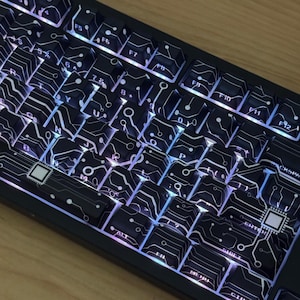 Könnte beinhalten: Eine schwarze mechanische Tastatur mit benutzerdefinierten Tastenkappen, die ein weißes Leiterplattenmuster aufweisen. Die Tasten zeigen alphanumerische Zeichen und Funktionsbeschriftungen, mit weißer Hintergrundbeleuchtung zwischen den Tasten.