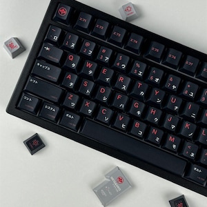 May include: A black mechanical keyboard featuring dark keys with red lettering, including Latin characters and Japanese katakana. Several loose gray and black keycaps with red symbols and the text Arasaka are scattered around the keyboard frame.