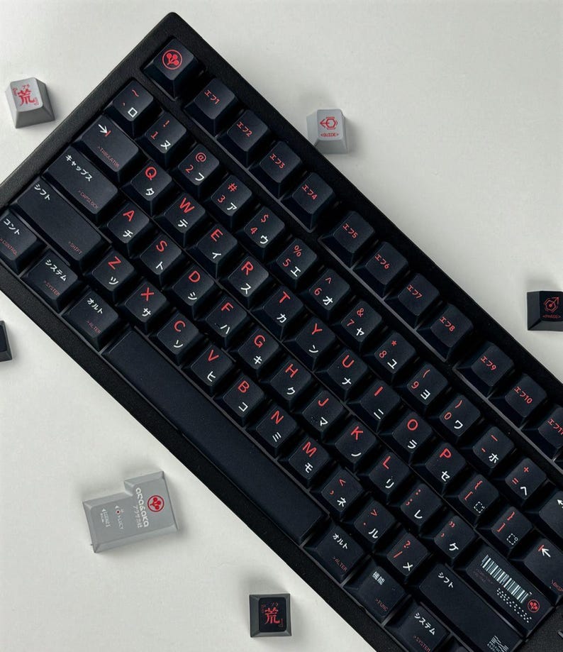 May include: A black mechanical keyboard featuring red alphanumeric characters and Japanese katakana legends on each keycap. Several loose gray and black keycaps with red symbols and text are scattered around the main keyboard unit.