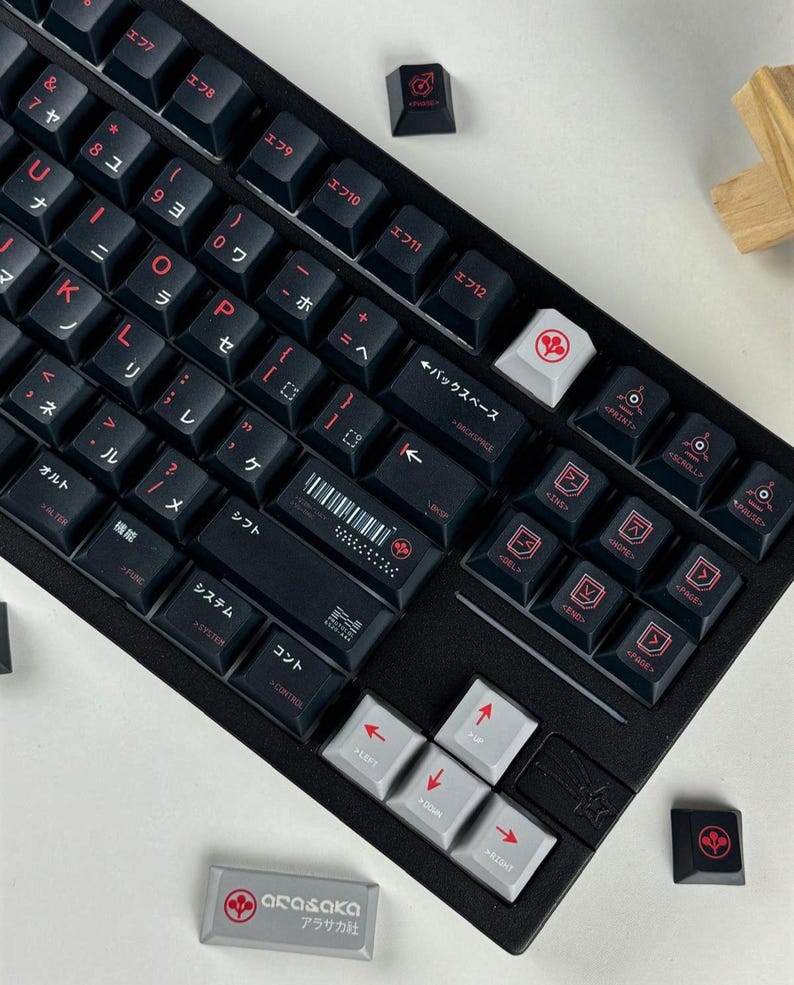 May include: A black mechanical keyboard featuring dark keycaps with red Japanese characters and English sub-legends. The layout includes a white backspace key, light gray arrow keys, and a rectangular gray spacebar with the Arasaka logo and text.