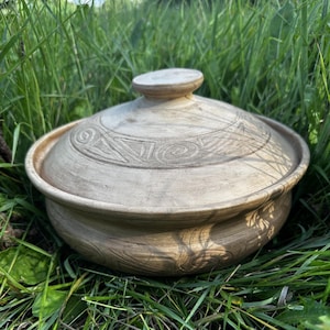 May include: A round, light brown ceramic lidded pot featuring a smooth, matte finish and hand-carved geometric patterns, including spirals and triangles, etched into the surface of both the lid and the main body of the vessel.