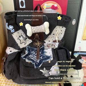 May include: A dark gray canvas backpack featuring white fabric patches with black stars, a plush bone-shaped accent, a cat face graphic, and a blue denim star patch. The bag includes brown leather-like straps and metal hardware. Dimensions are 30 cm by 42 cm.