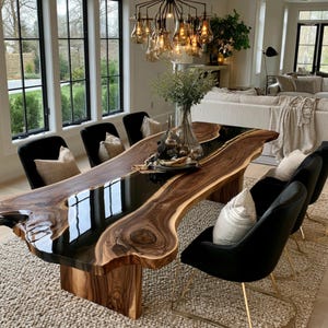 May include: A live edge dining table featuring a dark wood slab with a central black resin inlay, supported by a matching wood base. The table is surrounded by six black upholstered chairs with gold-toned metal legs and light-colored throw pillows.