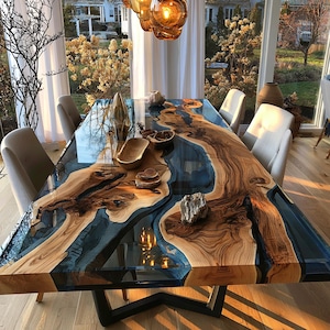Puede incluir: Una mesa de comedor rectangular con un tablero de madera de borde natural y un río central de resina azul translúcida. La mesa se apoya sobre una base de metal negro y está rodeada por seis sillas tapizadas con tela de color claro.