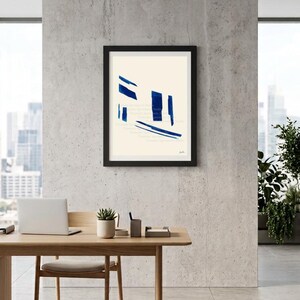 Puede incluir: Una lámina de arte mural enmarcada con fondo color crema y pinceladas azules abstractas y llamativas dispuestas en una composición geométrica. La obra está dentro de un marco negro sencillo, mostrando un diseño visual limpio y contrastado.
