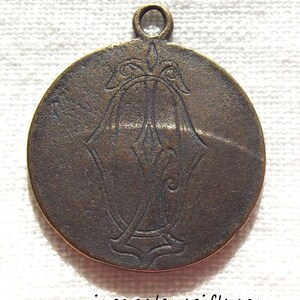 May include: A round, bronze-colored pendant with a decorative design. The pendant has a loop at the top for hanging.