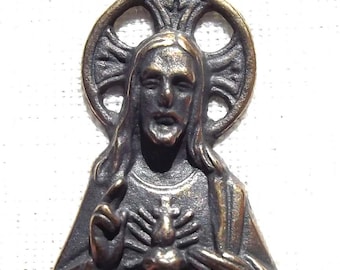Peut inclure: Un pendentif en bronze représentant Jésus-Christ avec son cœur exposé, entouré d'une auréole circulaire avec un motif de croix.