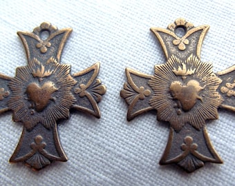 Peut inclure: Deux croix anciennes en bronze avec un motif de cœur et de flammes. Les croix sont ornées et présentent un design détaillé.