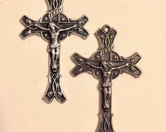 Peut inclure: Deux crucifix argentés avec une finition noire. Chaque crucifix représente une figure de Jésus-Christ sur la croix. Les croix ont des motifs ornés et les mots "INRI" en haut.