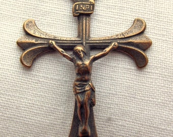 Op de afbeelding: Een bronzen kruisbeeld met een gedetailleerd beeld van Jezus Christus aan het kruis. Het kruis heeft een fleur-de-lis-ontwerp aan de boven- en onderkant en het opschrift "INRI" op de dwarsbalk.