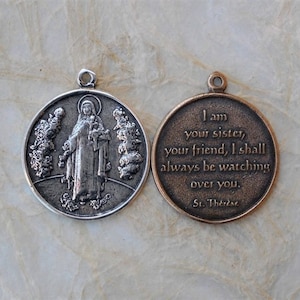 Op de afbeelding: Een zilveren en bronzen medaille met een afbeelding van Sint Theresia van Lisieux aan de ene kant en een citaat van haar aan de andere kant. Het citaat luidt: "Ik ben je zus, je vriendin, ik zal altijd over je waken. Heilige Theresia."