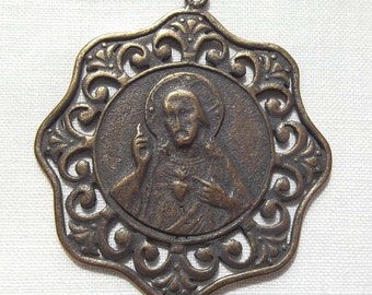 Peut inclure: Un pendentif en bronze représentant une image détaillée de Jésus-Christ avec son cœur exposé et une couronne d'épines. Le pendentif est entouré d'un cadre décoratif et orné.