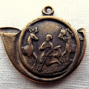 May include: A bronze pendant in the shape of a hunting horn with a circular medallion depicting a kneeling figure with a deer and a dog on either side.