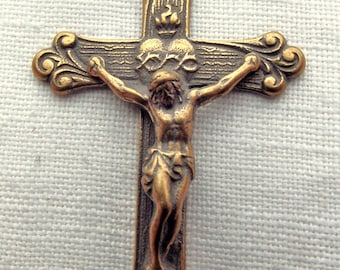 Op de afbeelding: Een gouden metalen kruisbeeld met een gedetailleerd beeld van Jezus Christus op het kruis. Het kruis heeft sierlijke bloemmotieven aan de boven- en onderkant.