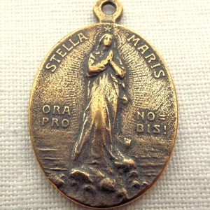 Op de afbeelding: Een gouden metalen hanger met een afbeelding van de Maagd Maria met de woorden "Stella Maris" en "Ora Pro Nobis" rond de rand.