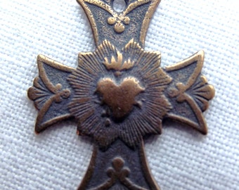 Peut inclure: Un pendentif en forme de croix en métal de couleur bronze avec un motif en forme de cœur au centre. Le cœur est entouré d'un motif en forme de soleil et la croix présente des détails ornés.