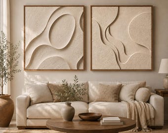 May include: Two square wall art pieces featuring raised, textured beige plaster in abstract organic shapes, each encased in a thin wooden frame. The artwork displays smooth, flowing curves and deep shadows, creating a three-dimensional effect.