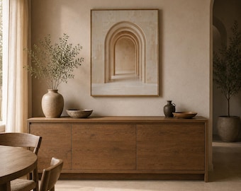 May include: A rectangular wall art print featuring a series of receding beige stone arches, framed in a thin gold border. The artwork is displayed above a long, dark brown wooden sideboard with three cabinet doors and a smooth, flat top surface.