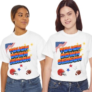 Op de afbeelding: Een wit t-shirt met korte mouwen en de tekst TOUCH DOWN SEASON in een blauw, oranje en rood kleurverloop. Het ontwerp bevat een afbeelding van een Amerikaanse vlag, een rode footballhelm, een bruine football en diverse kleine sterren.