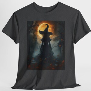 Op de afbeelding: Een antracietgrijs T-shirt met korte mouwen en een rechthoekige grafische print van een silhouetfiguur met een puntige heksenhoed. De scène toont een donker, mistig bos met een grote, gloeiende oranje volle maan en herfstbladeren.