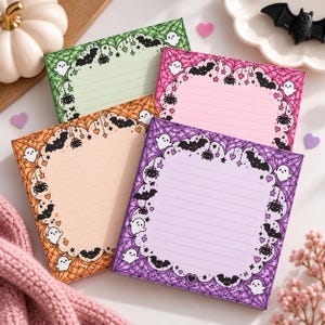 May include: Four square lined sticky note pads in green, pink, orange, and purple. Each pad features a decorative border with illustrations of ghosts, bats, spiders, hearts, and spiderwebs. The paper is lined for writing notes or lists.