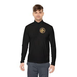 May include: A black long-sleeved quarter-zip pullover featuring a circular emblem on the left chest. The emblem displays a gold-toned wolf head profile inside a double-lined circle. The garment has a high collar and long sleeves with fitted cuffs.