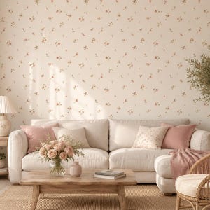 May include: A cream-colored sofa with pink and beige throw pillows, positioned in front of a wall covered in floral wallpaper with small pink and brown blossoms. A wooden coffee table sits in front, holding a glass vase filled with pink roses.
