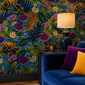 Pode incluir: Um sofá de veludo azul com uma almofada roxa e uma almofada amarela, posicionado contra um papel de parede com padrão de leopardos, macacos e flores roxas e brancas. Um candeeiro de mesa com base escura e cúpula branca está numa mesa.