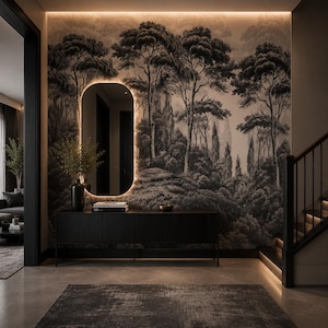 May include: A black console table with vertical slats sits against a wall featuring a large, monochromatic forest mural. Above the table, an oval mirror with integrated backlighting reflects the space. A dark vase and books rest on the surface.
