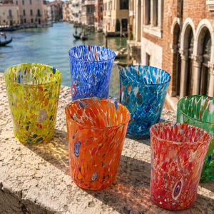 Könnte beinhalten: Ein Set aus sechs Trinkgläsern mit einem gesprenkelten, mehrfarbigen Konfetti-Muster. Das Set enthält einzelne Becher in leuchtenden Farben wie Gelb, Blau, Orange, Hellblau, Rot und Grün, die jeweils ein einzigartiges, mundgeblasenes Aussehen haben.