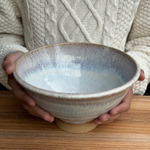May include: A white ceramic bowl with a light brown rim and a light brown base. The bowl has a speckled glaze and is slightly wider at the top than the bottom.