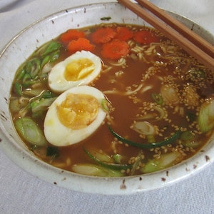 May include: A bowl of ramen with noodles, broth, carrots, green onions, sesame seeds, and two soft-boiled eggs.