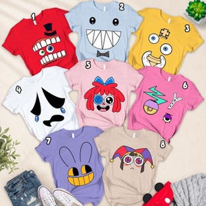 May include: Eight short-sleeved t-shirts in various colors, each featuring a unique character face graphic. The shirts are red, light blue, yellow, white, pink, magenta, purple, and beige, numbered one through eight for identification.