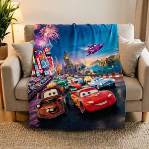 Op de afbeelding: Een rechthoekige fleece deken met een scène uit de film Cars, waarop Lightning McQueen en Takel op de voorgrond staan, met een stadsgezicht van Londen, de Big Ben en vuurwerk op de achtergrond onder een diepblauwe nachtelijke hemel.