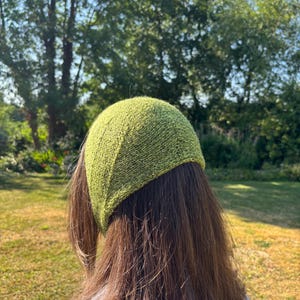 May include: A lime green knitted head covering with a textured stitch pattern. The accessory features a rounded shape that fits snugly over the crown of the head, showcasing a consistent knit construction with visible yarn loops throughout the fabric.