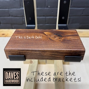 Puede incluir: Un estante de madera de roble oscuro con veta y nudo visibles, sostenido por dos soportes de metal negro. El estante presenta el texto 'This is Dark Oak!' y los soportes est&aacute;n etiquetados con el texto 'These are the included brackets!'.