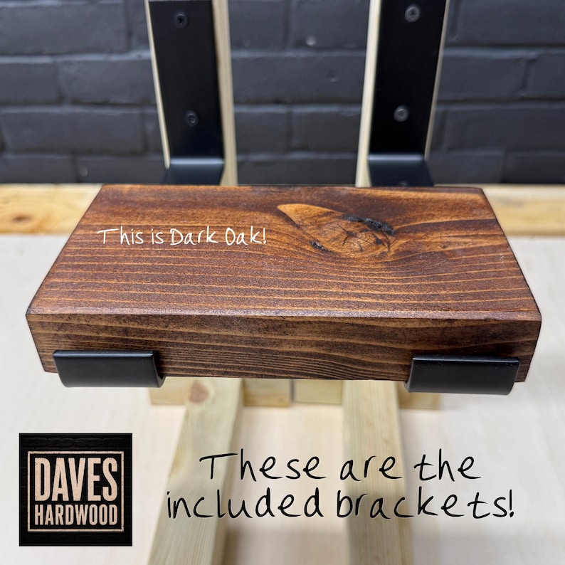 Puede incluir: Un estante de madera de roble oscuro con veta y nudo visibles, sostenido por dos soportes de metal negro. El estante presenta el texto 'This is Dark Oak!' y los soportes est&aacute;n etiquetados con el texto 'These are the included brackets!'.