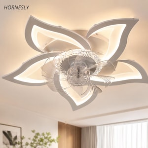 Puede incluir: Una lámpara de techo con ventilador en color blanco que presenta un diseño de flor de cinco pétalos con tiras de luz LED integradas. El centro incluye un ventilador circular con aspas transparentes rodeado por un anillo de cristales.