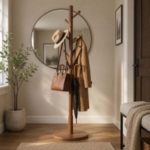 May include: A tall, dark brown wooden coat rack with a central pole and multiple rounded hooks. It holds a beige fedora, a brown leather handbag, a tan trench coat, and a black umbrella, all suspended from the various hooks on the stand.