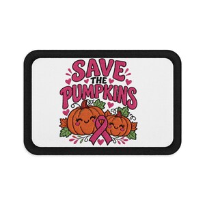 May include: A rectangular embroidered patch with a black border on a white background. It features the text "SAVE THE PUMPKINS" in pink, two smiling orange pumpkins with green leaves, and a pink awareness ribbon centered between them.