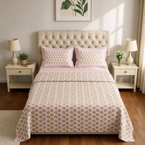 May include: A bed featuring a light pink quilt and two matching pillow shams, all decorated with a repeating green and pink floral block print pattern. The bed is positioned against a tufted beige headboard, creating a coordinated bedding set.